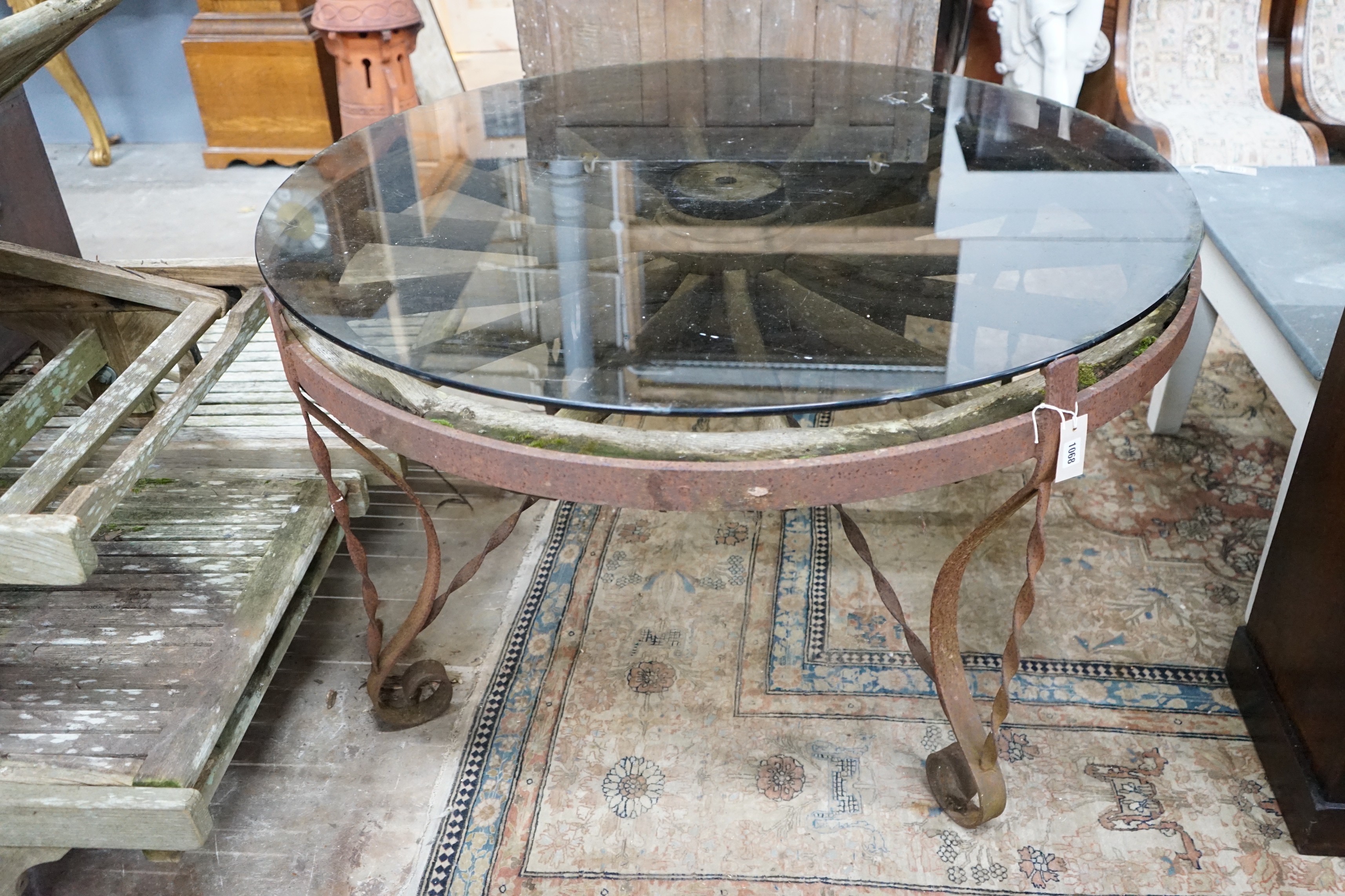 A wrought iron glass topped circular cartwheel garden table, diameter 124cm, height 72cm